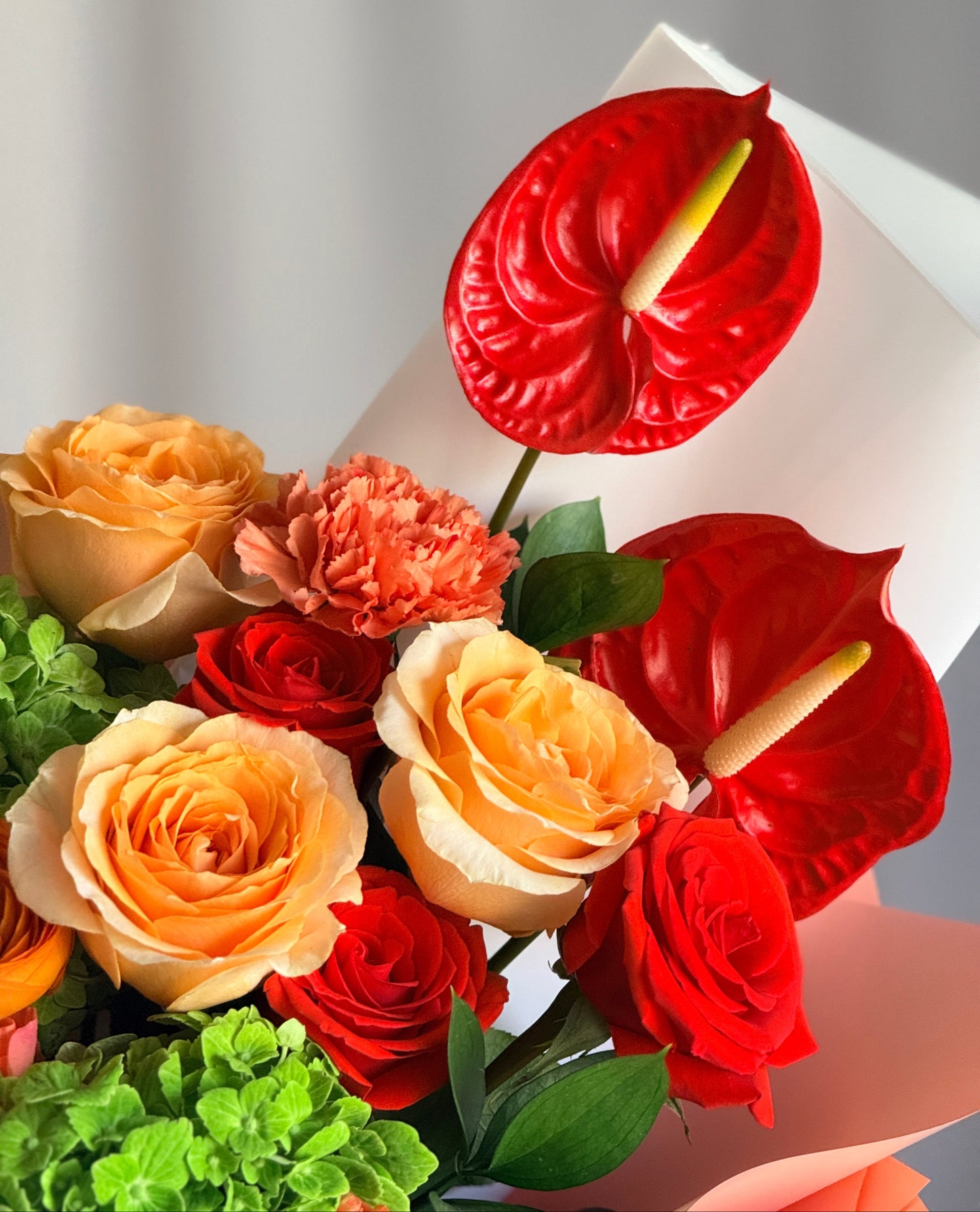 A bold, colorful bouquet of tropical anthuriums, sunset-colored roses, and vivid gerberas in a stylish designer wrap.