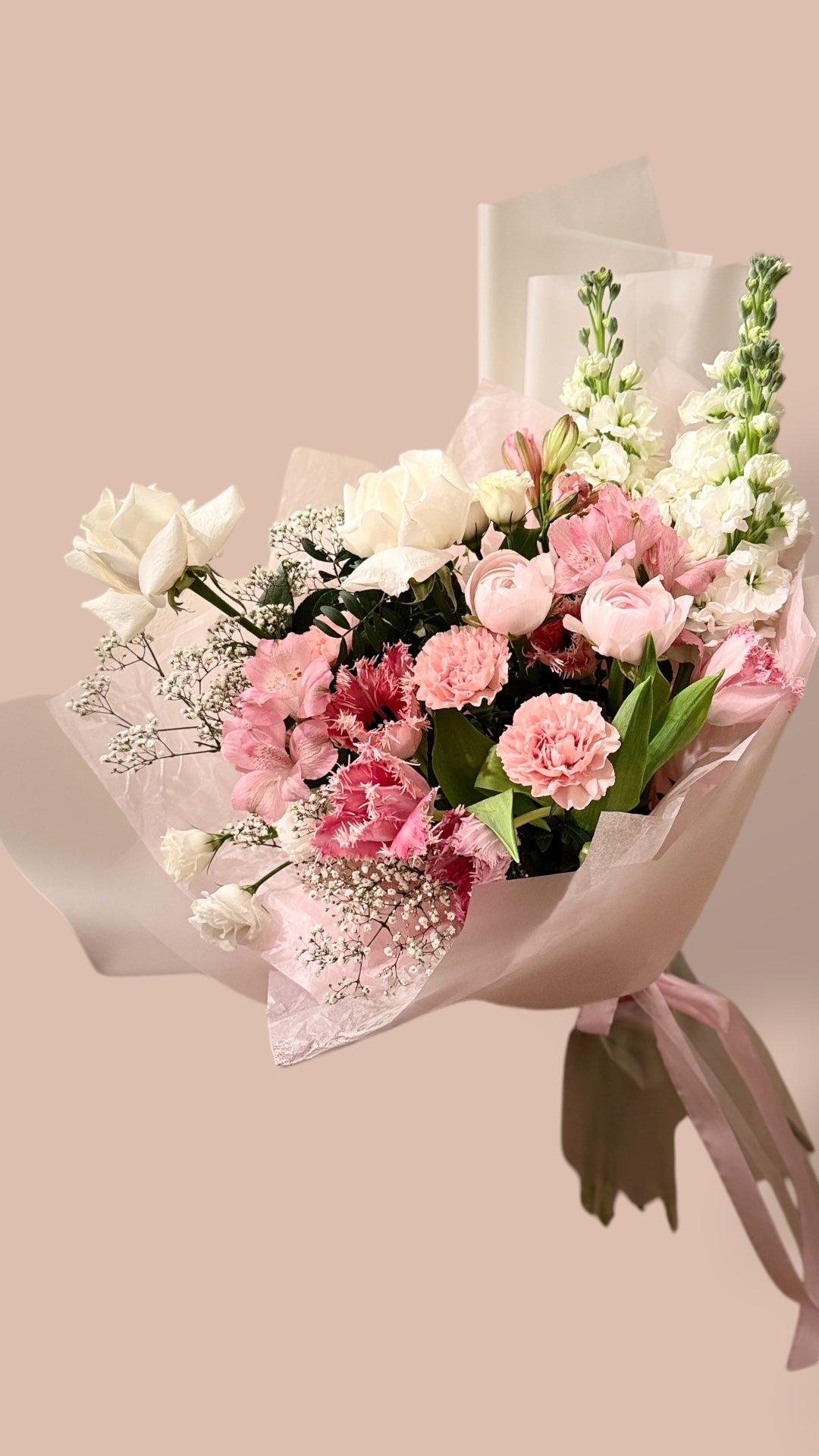 Delicate mixed bouquet with white roses, pink carnations, ranunculus, and white snapdragons, wrapped for flower delivery in Montreal.