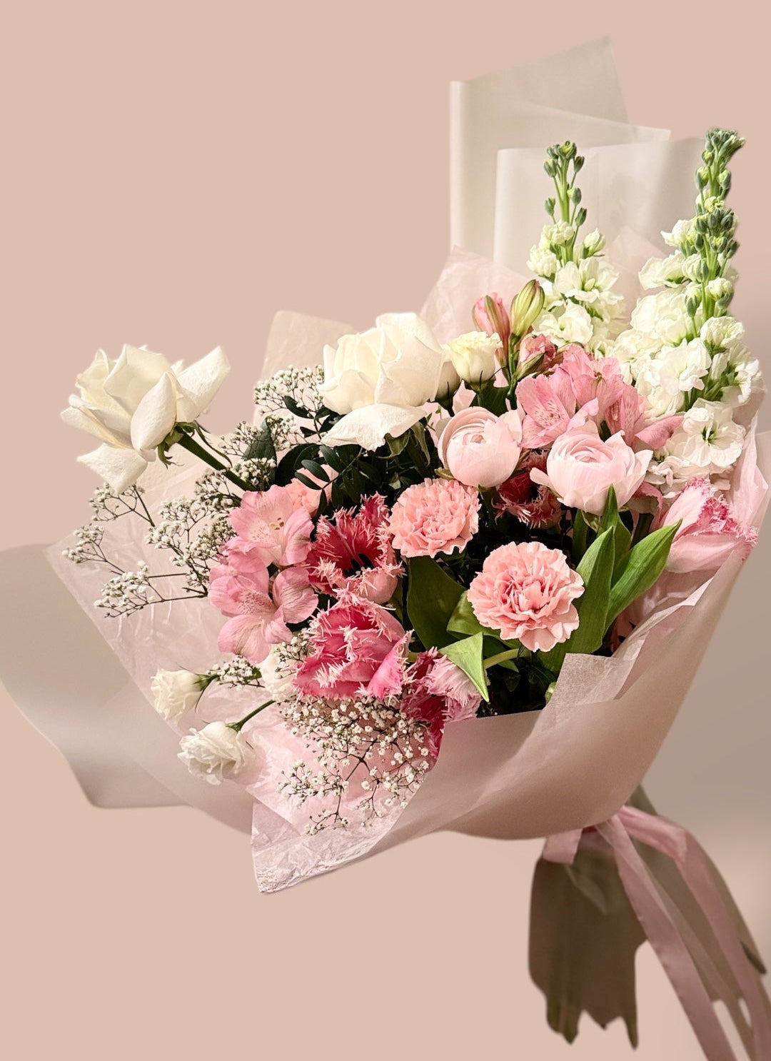 Delicate mixed bouquet with white roses, pink carnations, ranunculus, and white snapdragons, wrapped for flower delivery in Montreal.