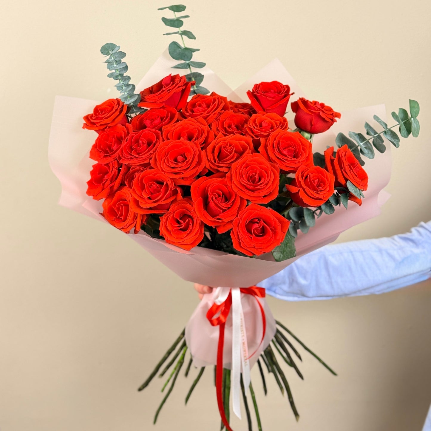 Bouquet of red roses with greenery held by a person against a beige background