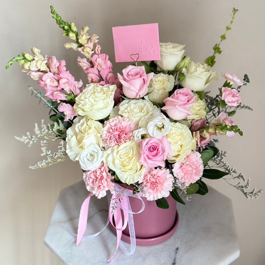 Bouquet of pink and white flowers in a pink box on a marble surface with a light gray background