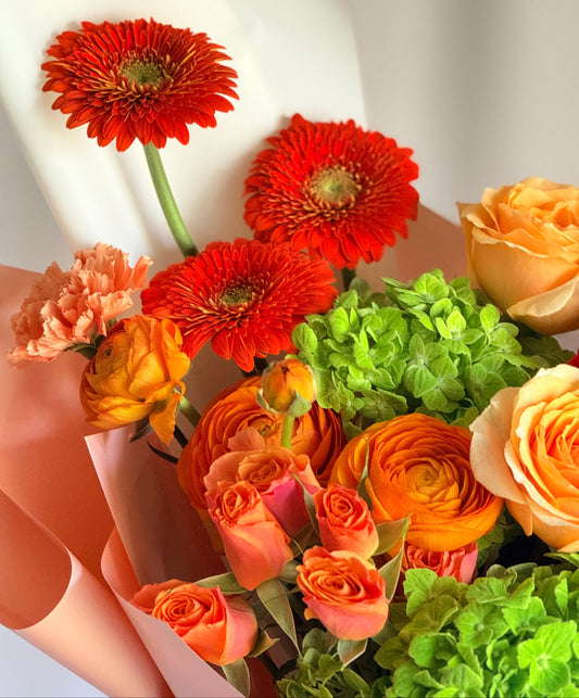 Bright and Juicy floral arrangement with red roses, orange ranunculus, and green hydrangea in a premium pink gift wrap—ideal for birthday or celebration flower delivery.