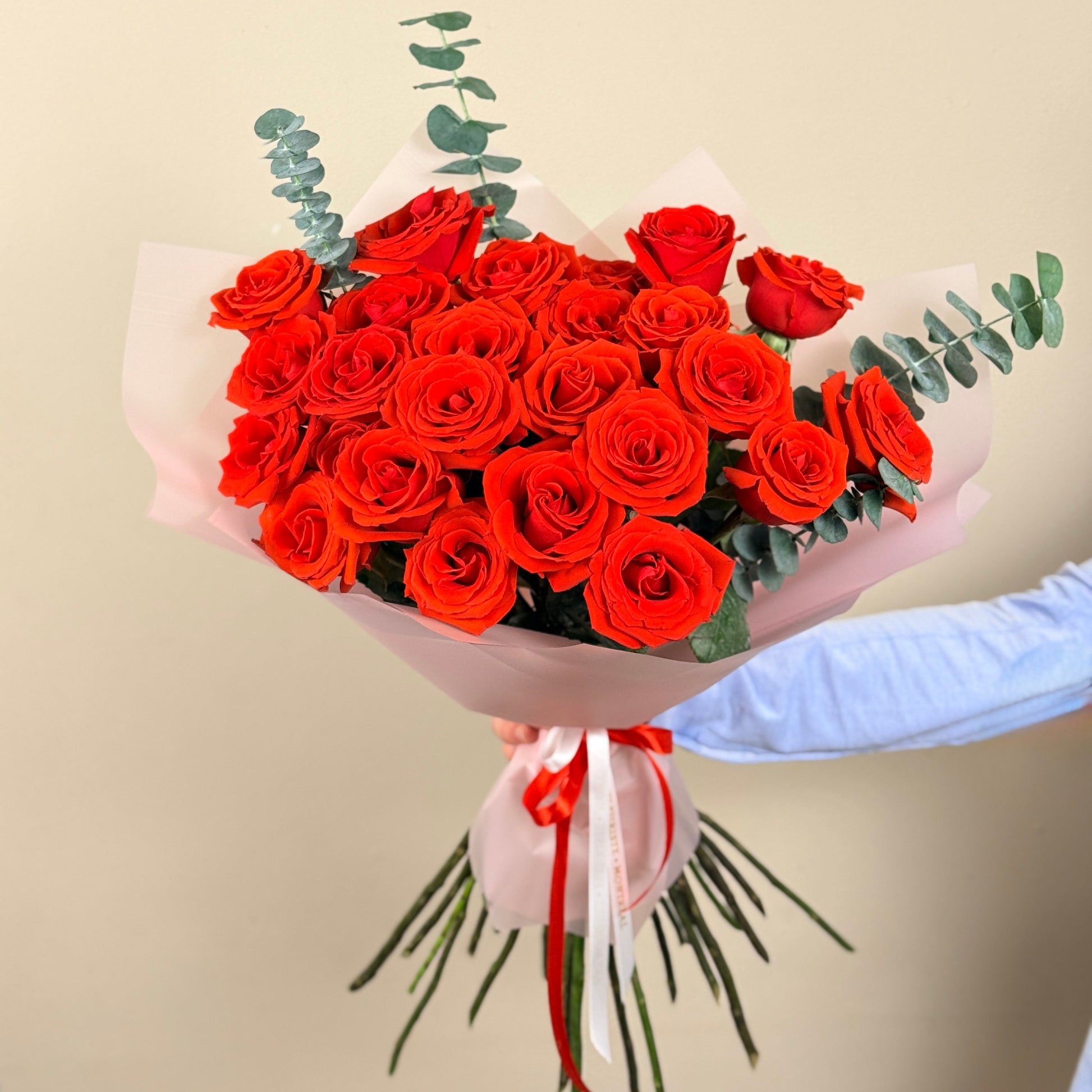Bouquet of red roses with greenery held by a person against a beige background