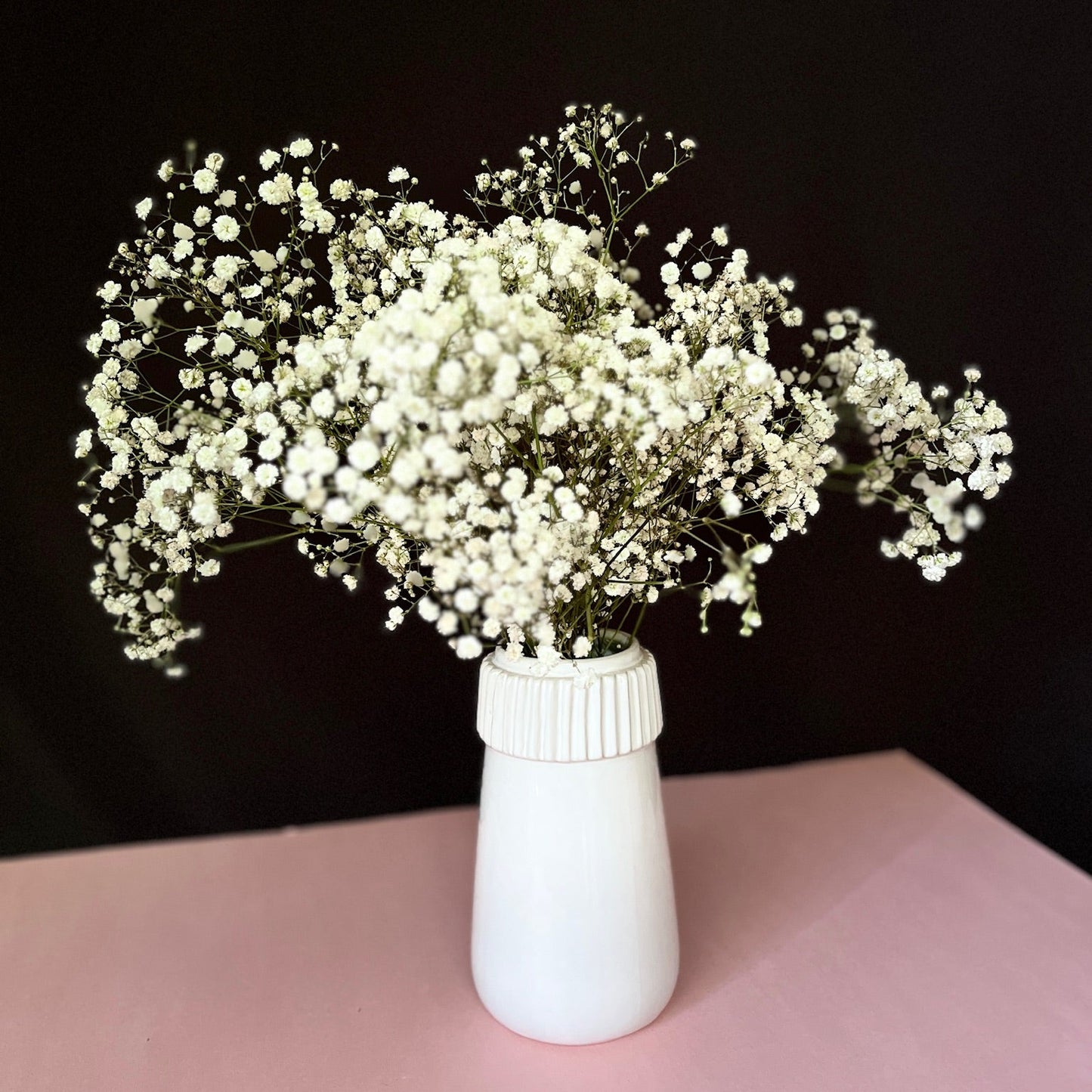 A white ceramic vase with a smooth, glossy finish, containing a bouquet of white flowers.